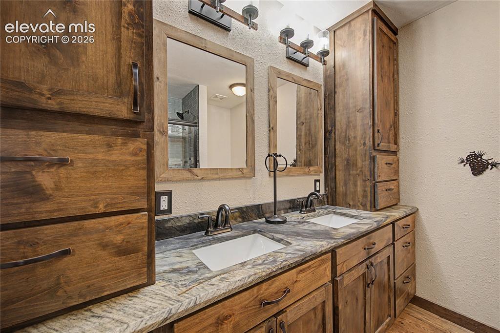 Image 32 of 46: Double vanity featuring wooden cabinetry, integrated sinks, and a stone cou