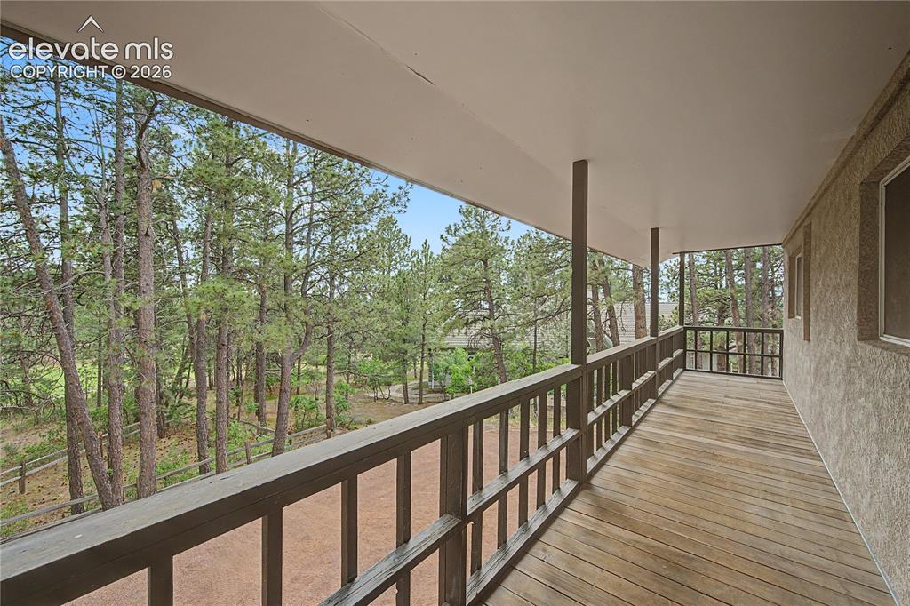 Image 38 of 46: Expansive covered porch featuring wood-finish decking, dark wood railings,