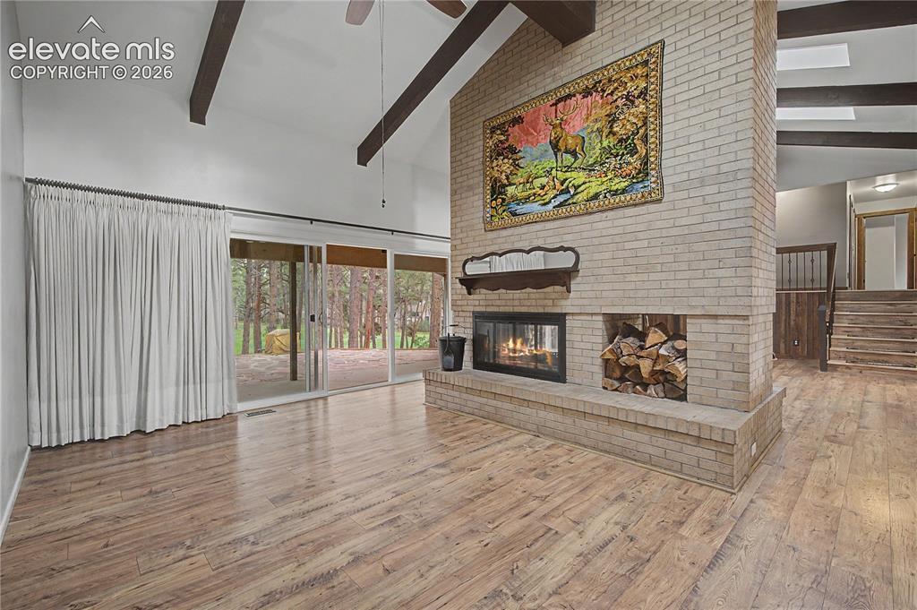 Image 7 of 46: Spacious room featuring vaulted ceilings with exposed wood beams, a brick f
