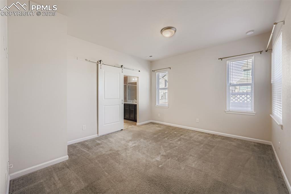 Image 14 of 30: Unfurnished bedroom featuring a barn door, multiple windows, carpet, and co