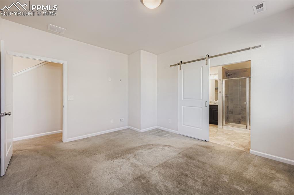 Image 15 of 30: Unfurnished bedroom with a barn door, light colored carpet, and connected b