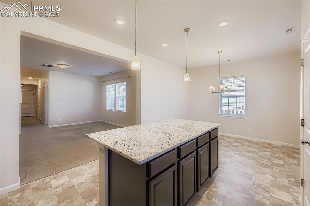 Image 9 of 30: Kitchen featuring decorative light fixtures, light stone countertops, open 