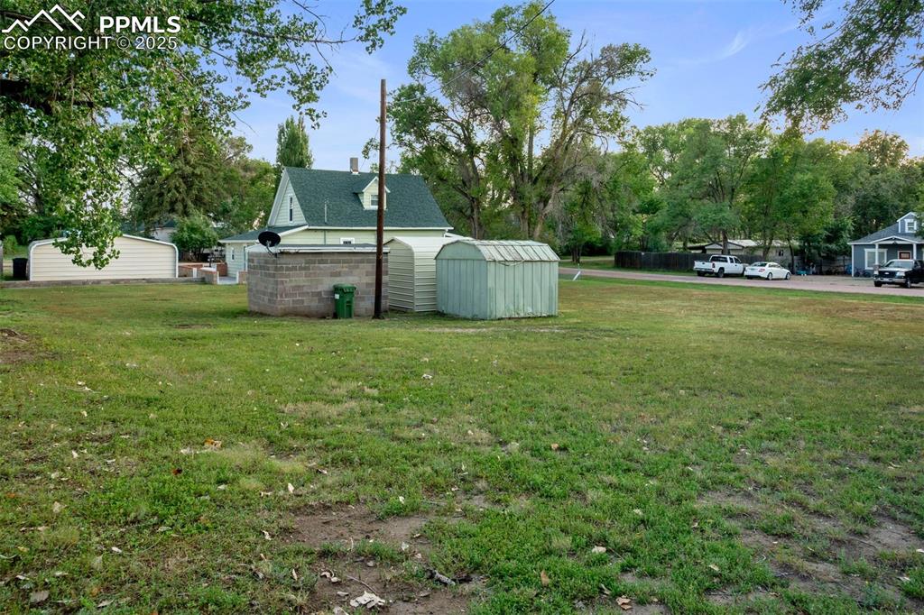 Image 23 of 24: View of grassy yard featuring an outdoor structure and view of wooded area