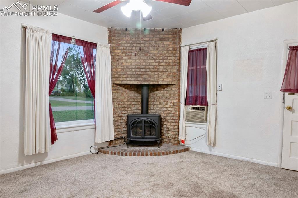 Image 3 of 24: Unfurnished living room featuring a wood stove, carpet, a ceiling fan, and