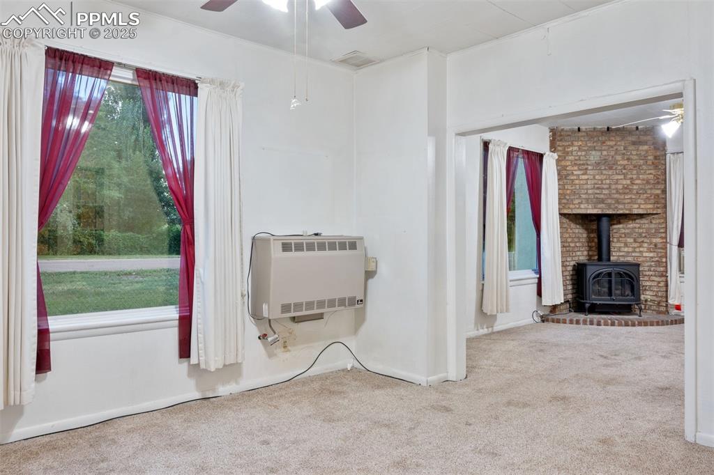 Image 4 of 24: Carpeted empty room with ceiling fan, a wood stove, and heating unit