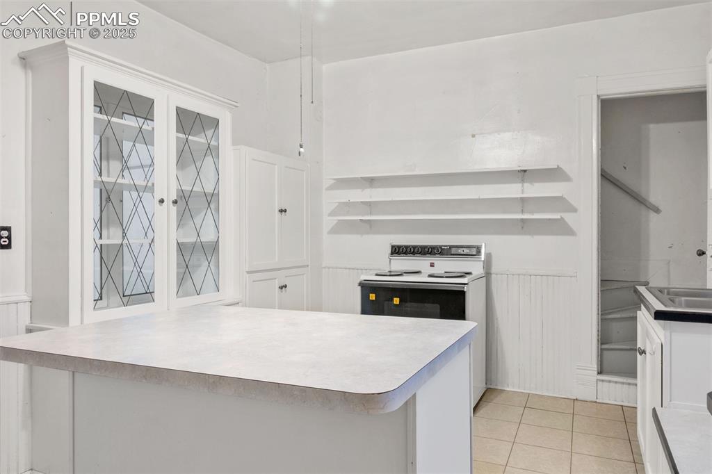 Image 8 of 24: Kitchen with white cabinetry, light tile patterned floors, white range with