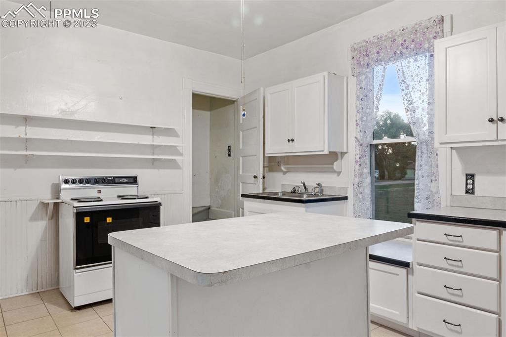 Image 9 of 24: Kitchen featuring white cabinetry, white electric stove, light tile pattern