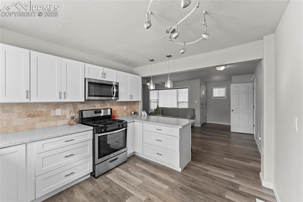 Image 12 of 24: Kitchen with white cabinets, stainless steel appliances, decorative backspl