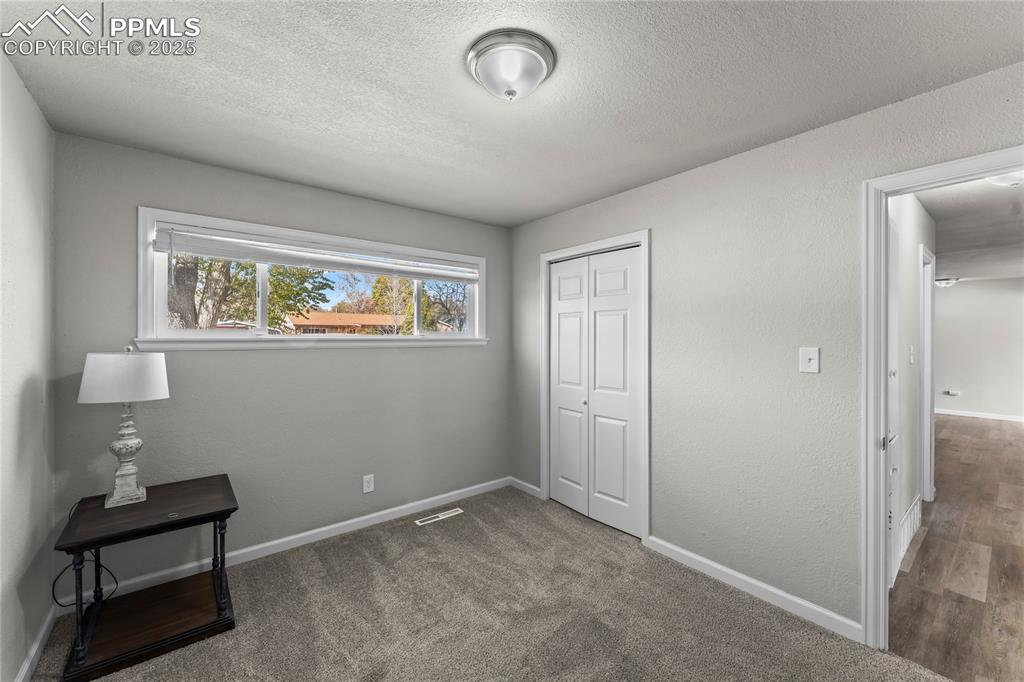 Image 19 of 24: Unfurnished bedroom with dark carpet, a closet, a textured wall, and a text