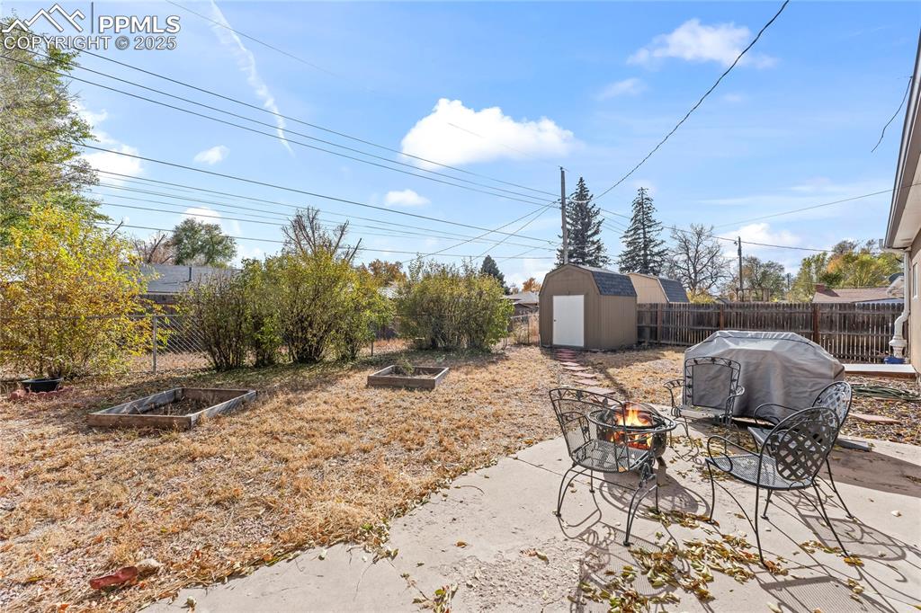 Image 20 of 24: Fenced backyard featuring a patio area, a fire pit, a storage unit, and a v