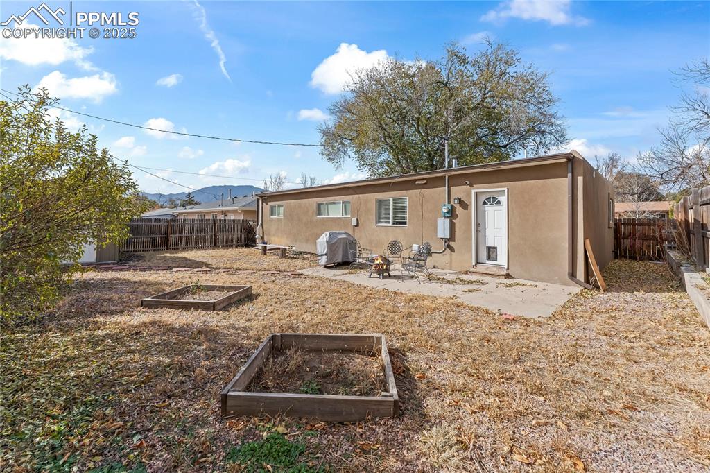 Image 21 of 24: Back of house featuring a patio, a vegetable garden, stucco siding, and a f