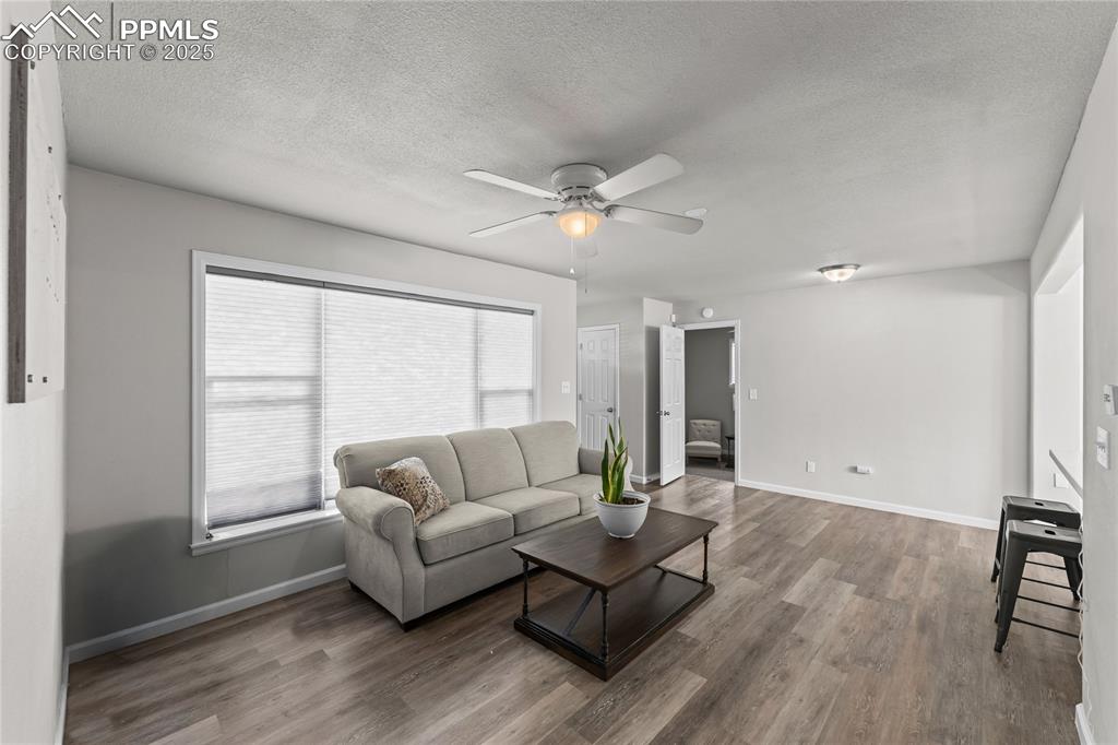 Image 4 of 24: Living area with a textured ceiling, wood finished floors, and ceiling fan