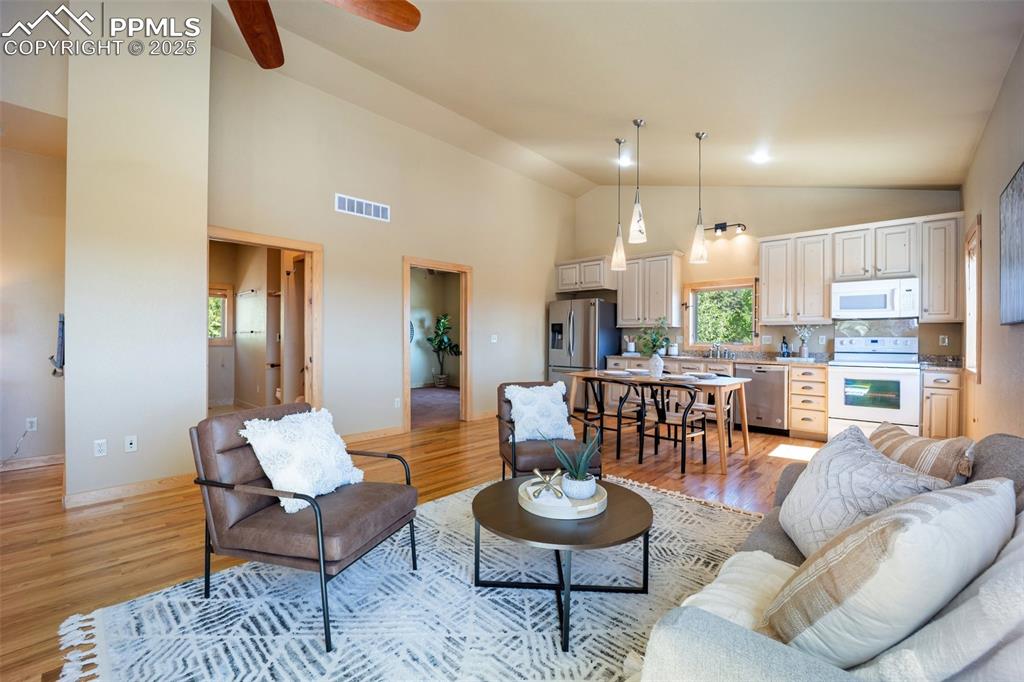 Image 8 of 50: Living area with light wood-style flooring, high vaulted ceiling, and a cei