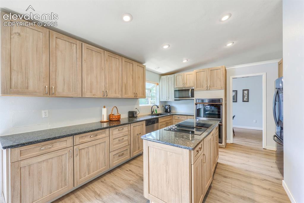 Image 10 of 42: Wood-finish cabinetry, dark countertops, central island with integrated coo