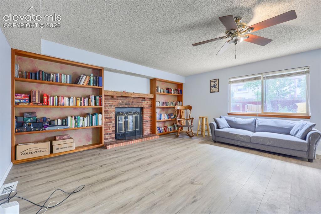 Image 12 of 42: LVP flooring, brick fireplace with a built-in mantel, integrated wood shelv