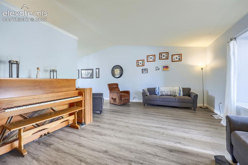 Image 19 of 42: Wood-finish flooring throughout, vaulted ceiling with crown molding, and li