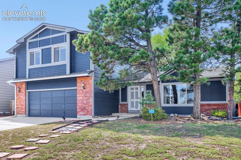 Image 2 of 42: Exterior featuring blue siding, brick accents, a two-car garage, and mature