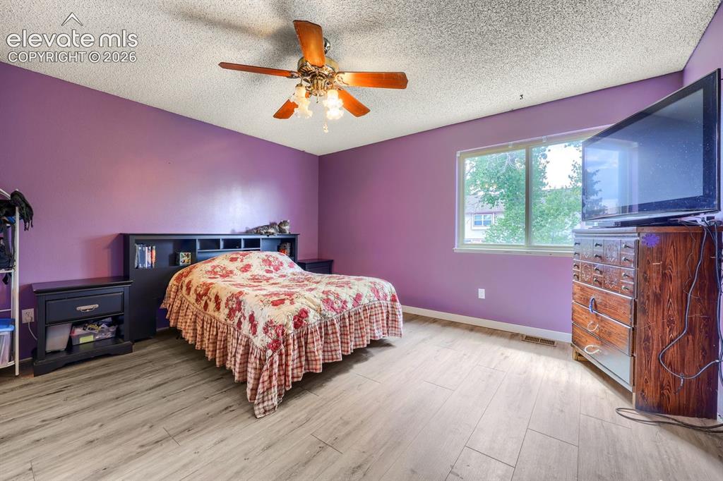 Image 22 of 42: Wood-finish flooring, ceiling fan with integrated lighting, built-in headbo