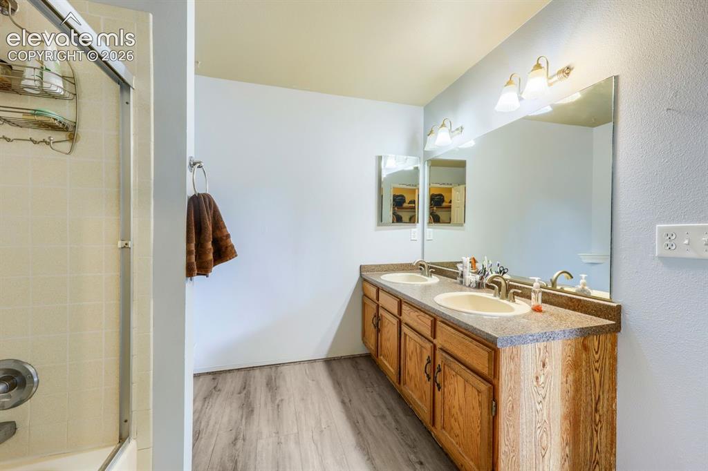 Image 26 of 42: Dual vanity with wood-finish cabinetry, integrated sinks, and a large wall-