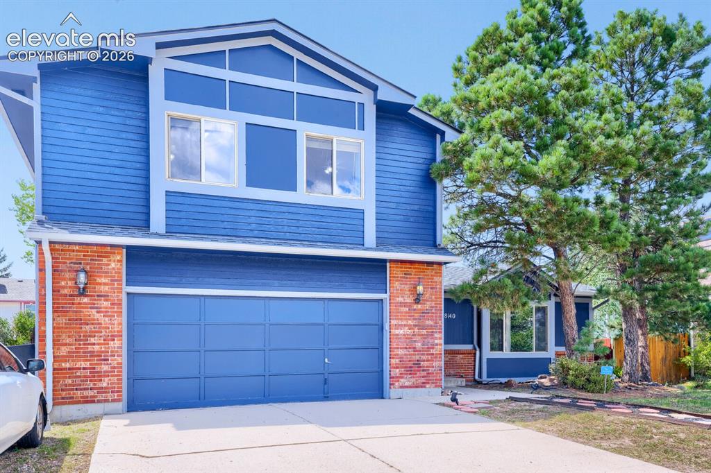 Image 32 of 42: Two-story exterior with blue siding, brick accents, a two-car garage, and m