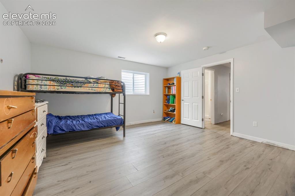 Image 34 of 42: Light wood-finish flooring, white walls, and a window with horizontal blind