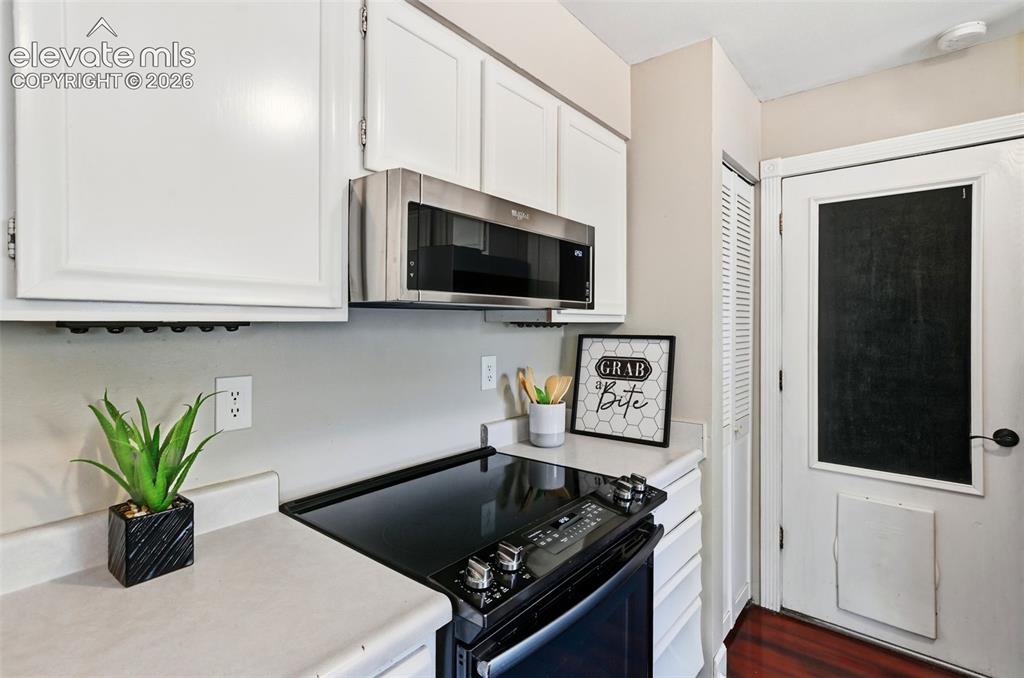Image 10 of 50: Kitchen featuring white cabinetry, a stainless steel microwave, a black ele
