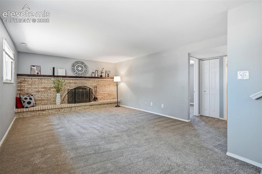 Image 15 of 50: Spacious living area featuring a light brick fireplace with a dark wood man