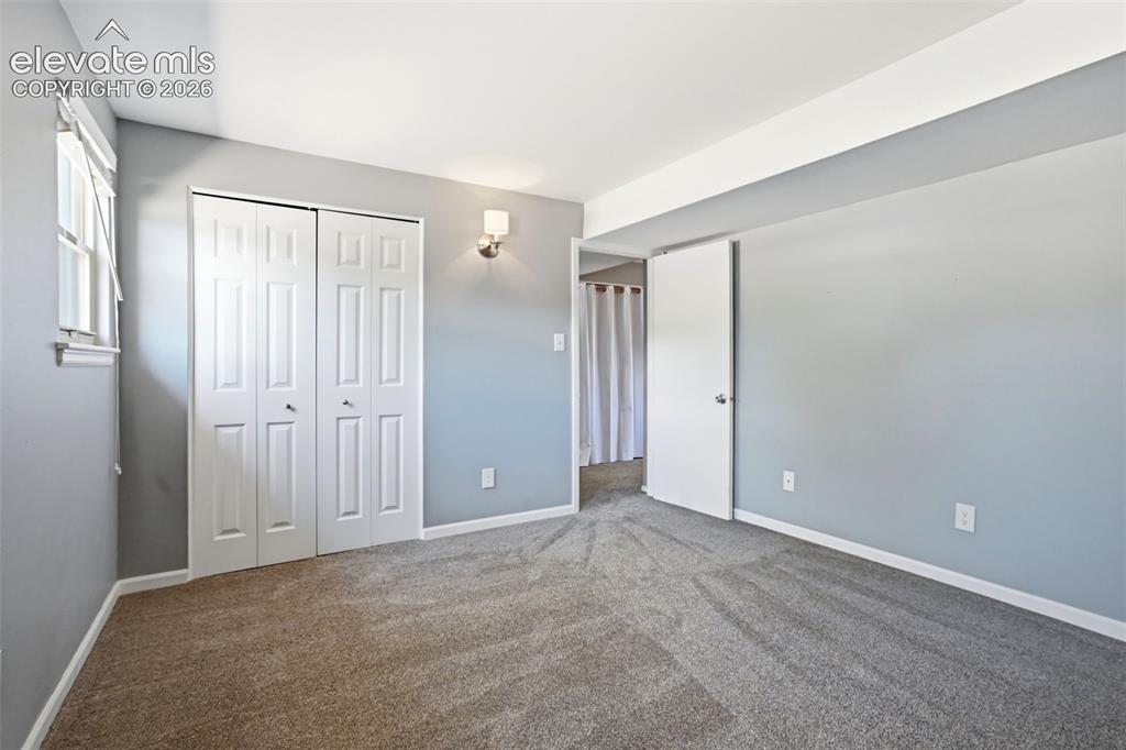 Image 23 of 50: Neutral tone walls and carpeting, featuring a window with blinds, bi-fold c