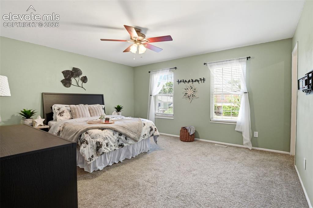 Image 29 of 50: Carpeted bedroom featuring two windows with blinds, a ceiling fan with ligh