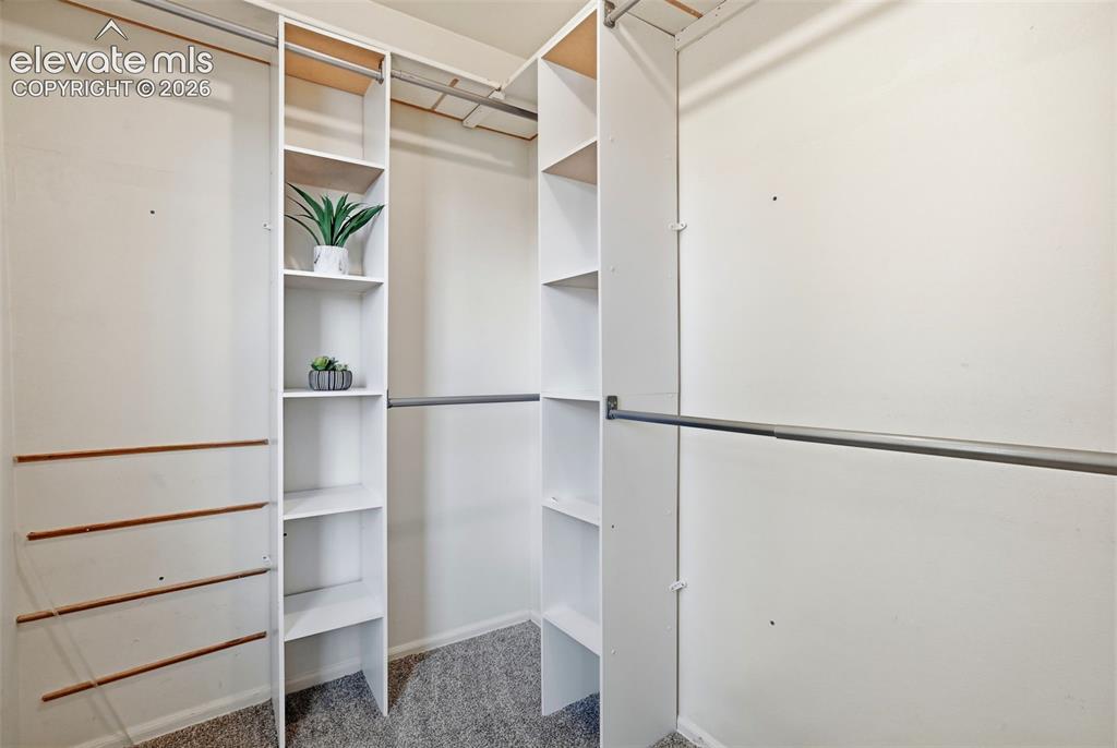 Image 33 of 50: Walk-in closet featuring built-in white shelving, multiple hanging rods, an