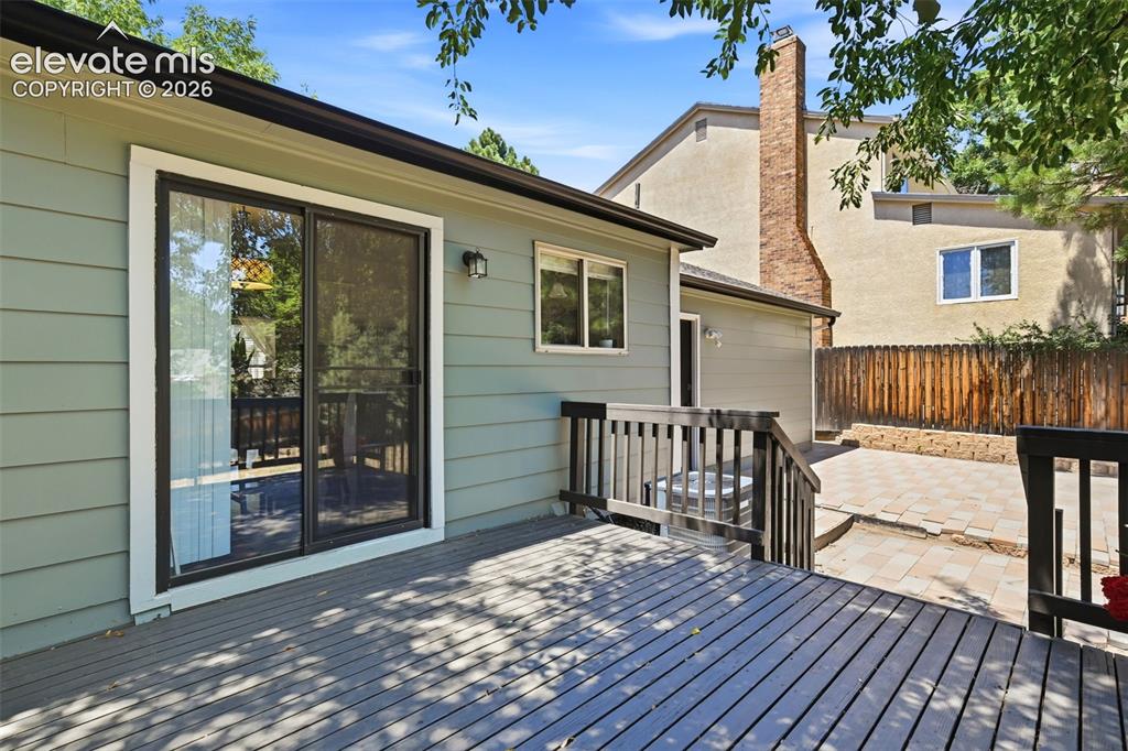 Image 35 of 50: Spacious wood deck with black railing, light green siding, and sliding glas