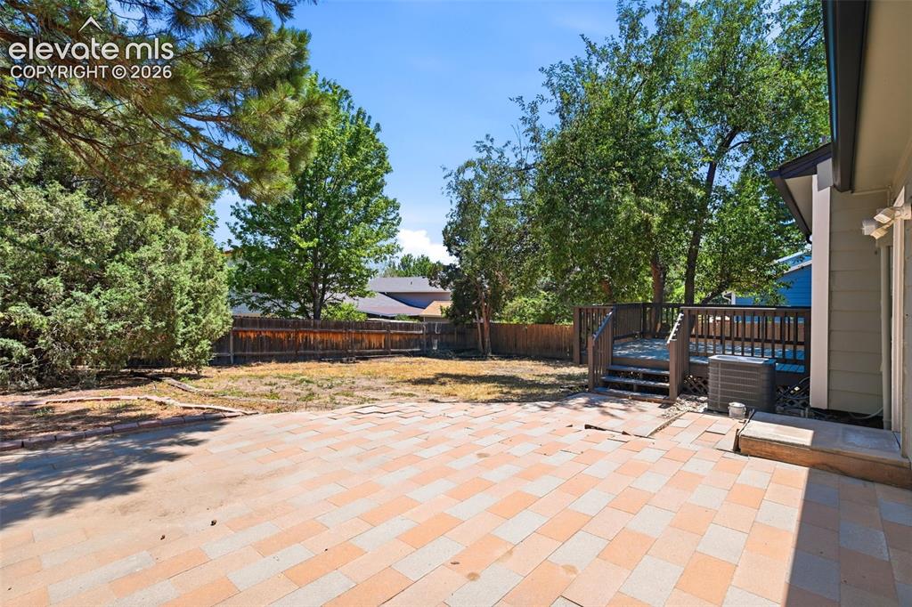 Image 36 of 50: Spacious backyard featuring a multi-toned paver patio, a wooden deck with r
