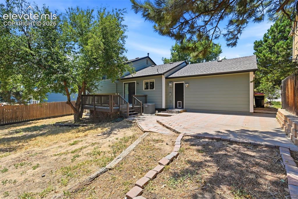 Image 37 of 50: Rear exterior featuring a wood deck, sliding glass door, and a paver patio