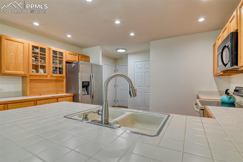 Image 12 of 43: Kitchen featuring tile counters, recessed lighting, stainless steel fridge,