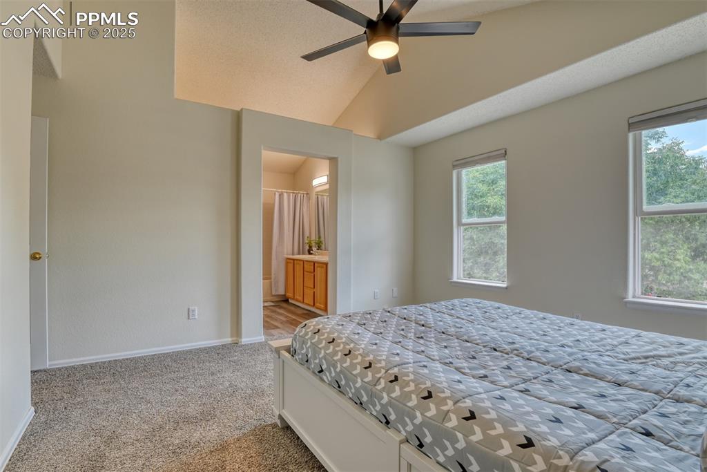 Image 19 of 43: Carpeted bedroom featuring vaulted ceiling, ensuite bath, and ceiling fan