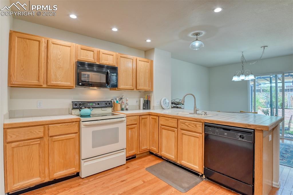 Image 9 of 43: Kitchen with tile counters, black appliances, light brown cabinetry, light