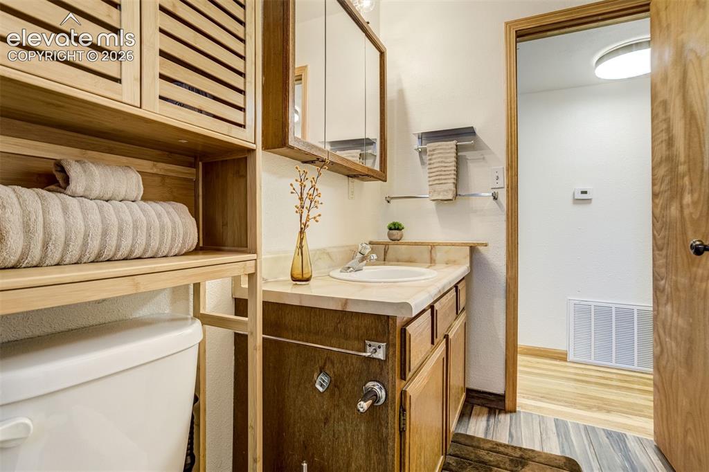 Image 25 of 31: Vanity with an integrated sink, wood-finish cabinetry, and a mirrored medic