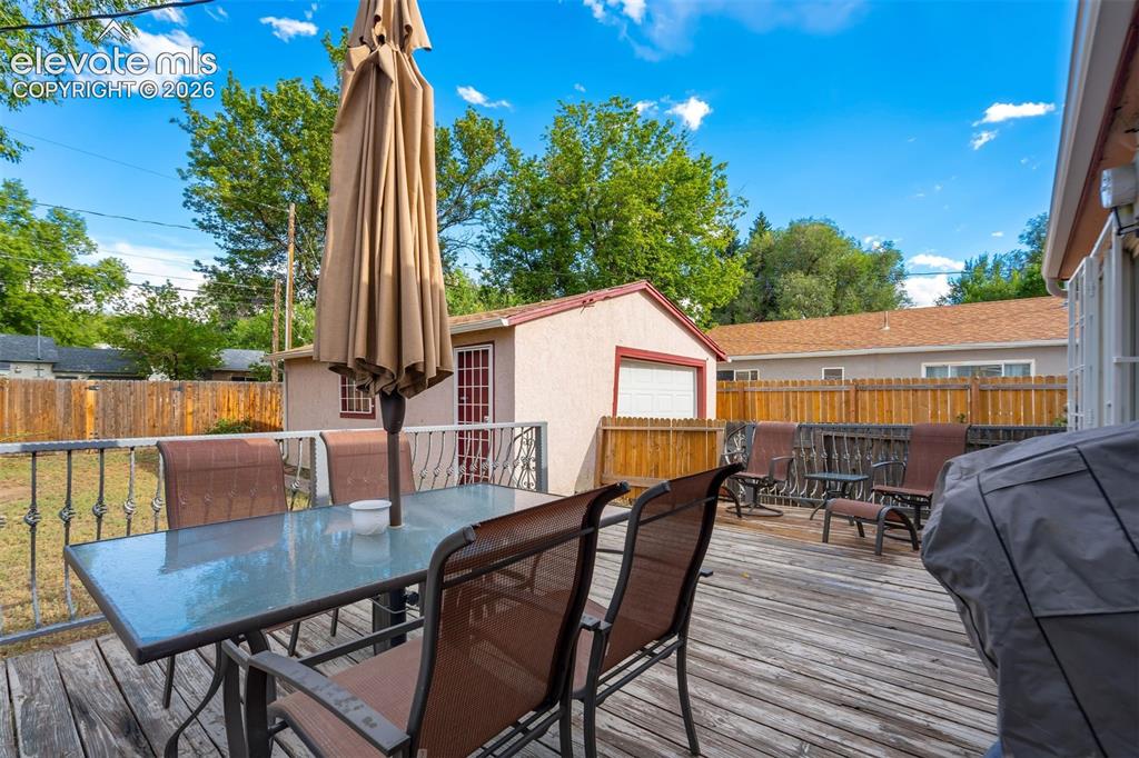 Image 26 of 31: Expansive wooden deck with black metal railings, a detached outbuilding wit