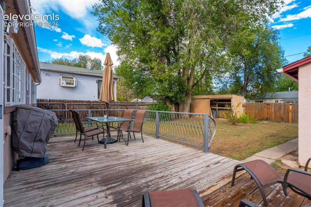 Image 27 of 31: Expansive wood deck with decorative metal railings, a grassy yard, and matu