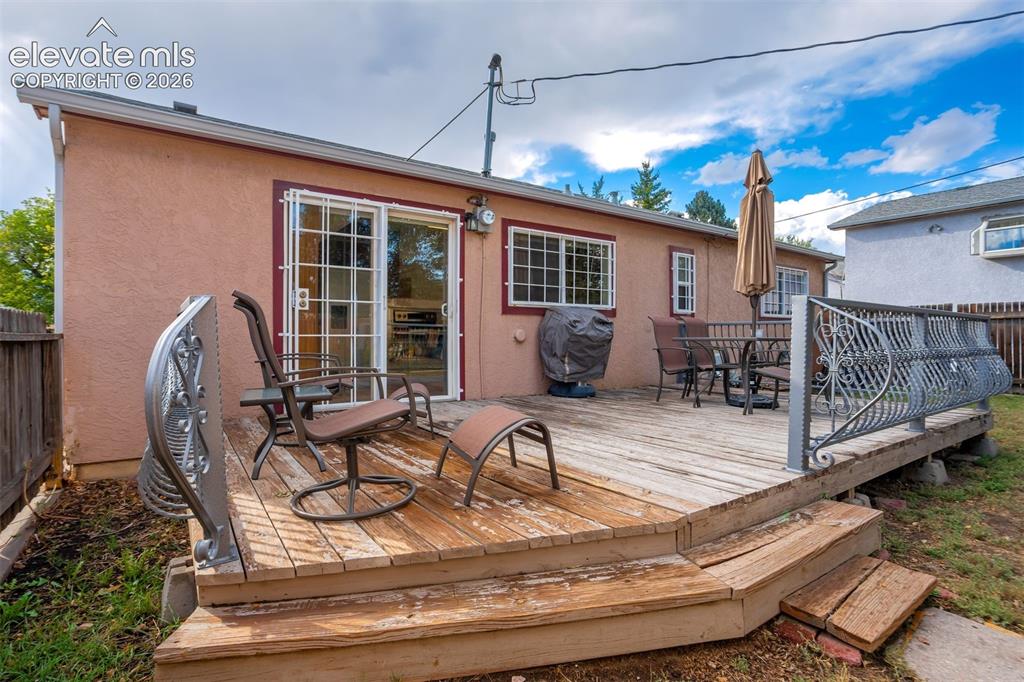 Image 28 of 31: Wood-plank outdoor deck with decorative metal railing and access to interio