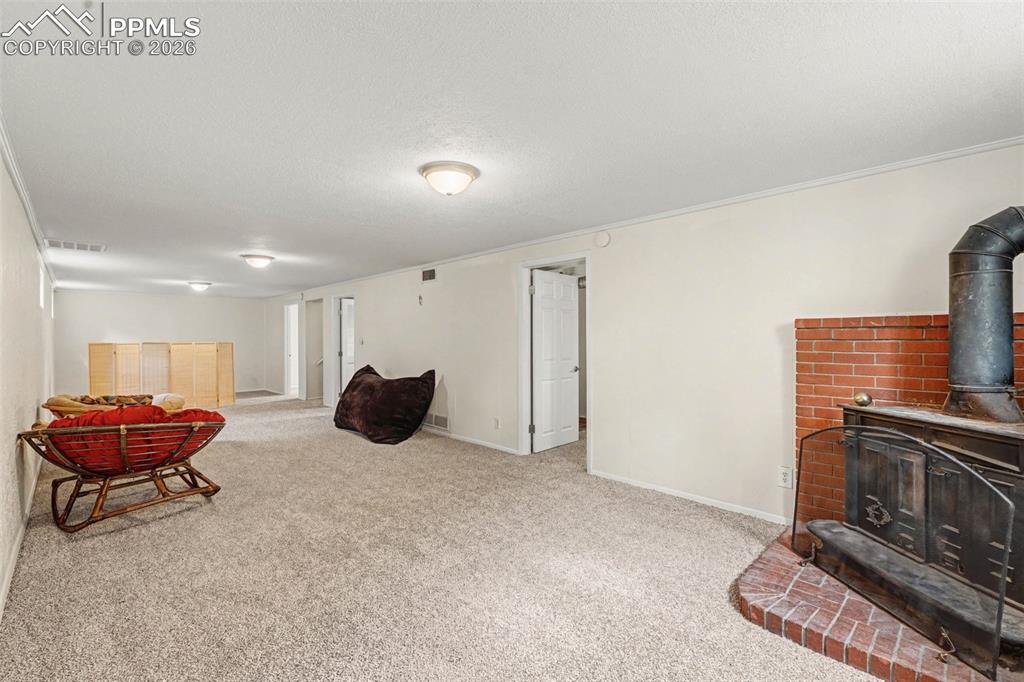 Image 11 of 23: Living room with a wood stove, ornamental molding, light carpet, and a text