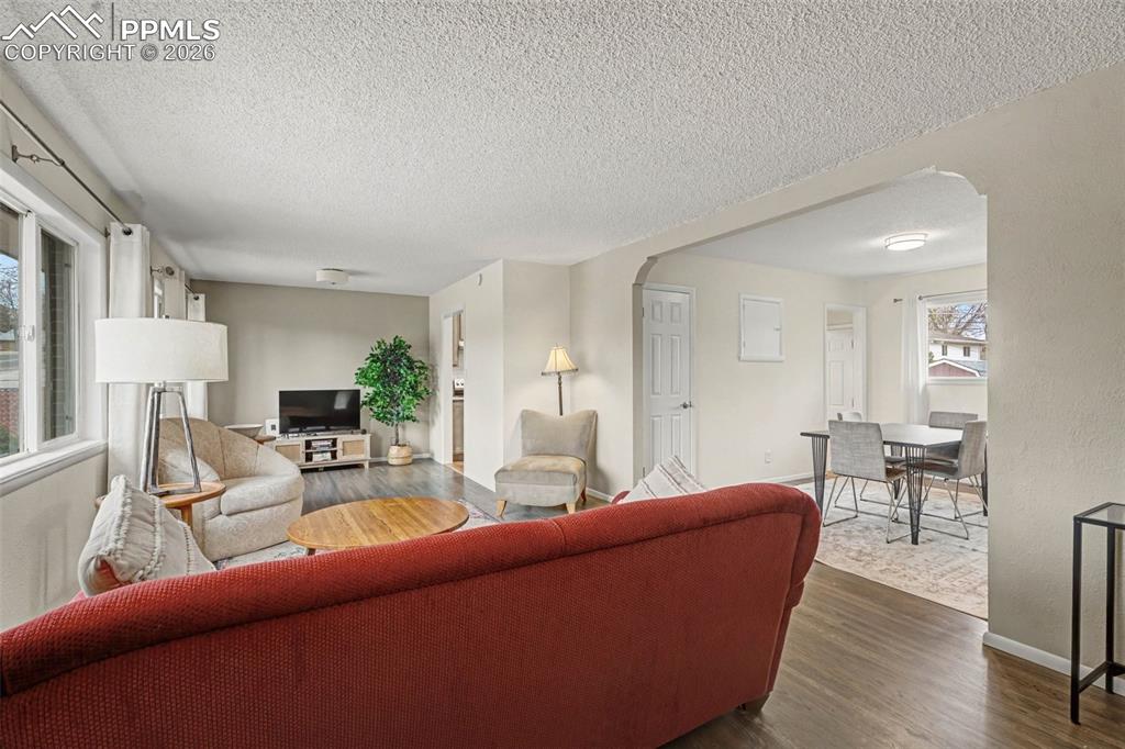 Image 3 of 23: Living room with arched walkways, dark wood-style floors, and a textured ce