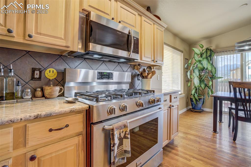 Image 12 of 50: Kitchen with light brown cabinets, stainless steel appliances, backsplash,