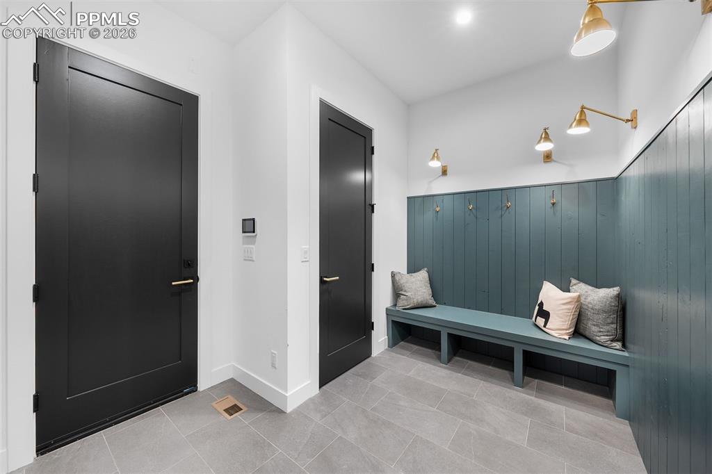 Image 33 of 37: Mudroom with built-in bench seating, vertical paneling, and brass hooks.