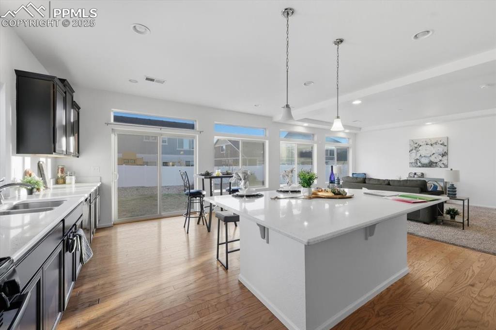 Image 16 of 41: Kitchen with light stone counters, pendant lighting, open floor plan, light