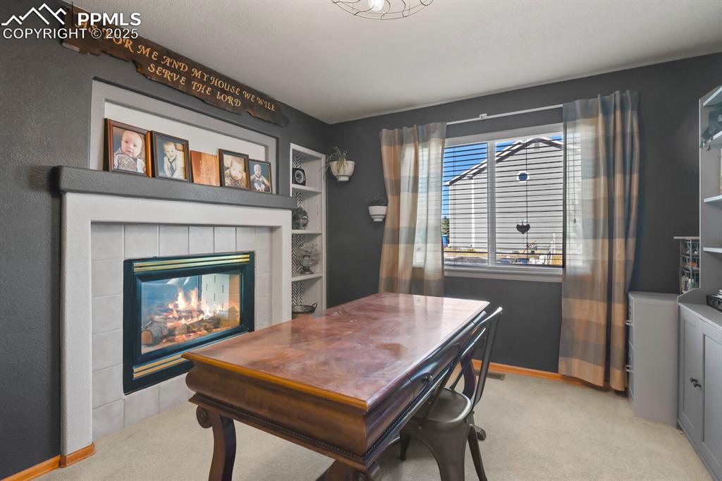 Image 19 of 50: Home office with light colored carpet, a tile fireplace, and built in shelv