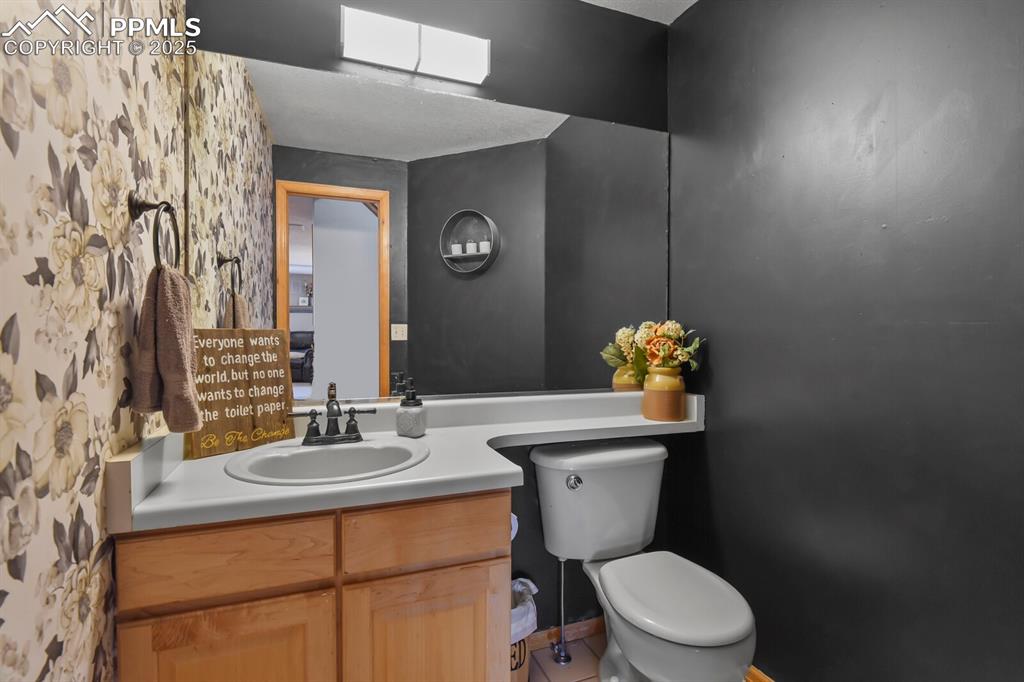Image 30 of 50: Half bathroom with vanity, wallpapered walls, a skylight, and tile patterne