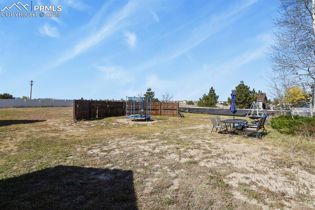 Image 39 of 50: Fenced backyard with a trampoline and outdoor dining area