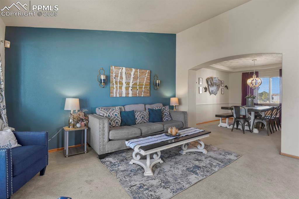 Image 5 of 50: Living room with arched walkways, carpet, and a chandelier