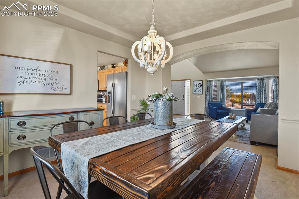 Image 8 of 50: Dining room with light colored carpet, arched walkways, and a chandelier